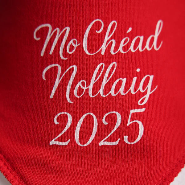 Red fabric with white text 'Mo Chéad Nollaig 2025' on a light  background