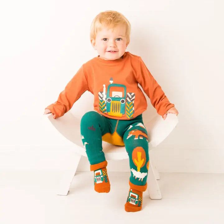 Child wearing an orange shirt with a truck design and green pants with animal prints, sitting on a white chair.