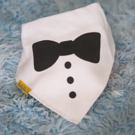 White bandana  bib with black bow tie and buttons on a textured blue background