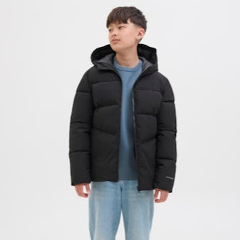 Boy wearing a black puffer jacket and light blue jeans on a white background