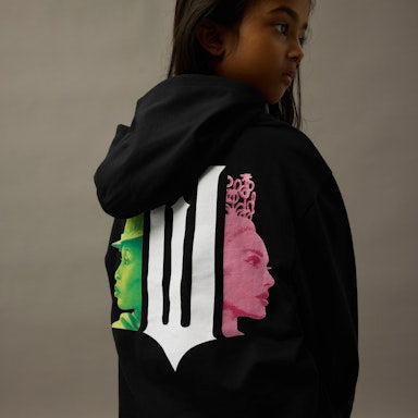 Girl wearing a black hoodie with Wicked logo designs on the back against a neutral background