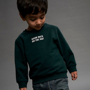 Child wearing a dark green sweatshirt with text on a grey background