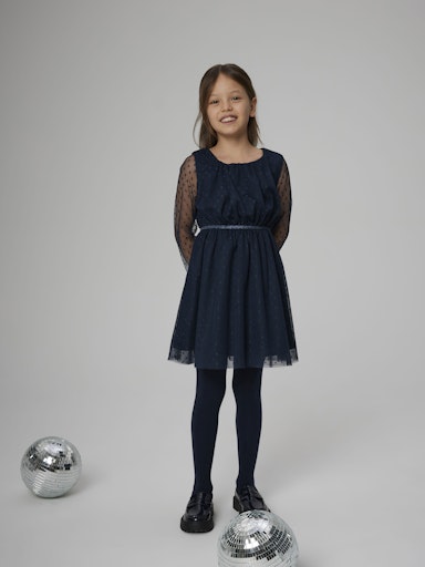 Young girl wearing a navy blue dress standing on a white background with disco balls.