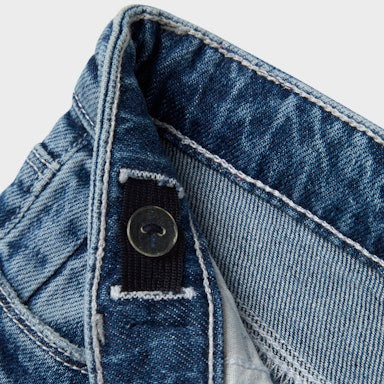 Close-up of a blue denim jeans with a button on a light grey background