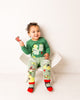 Child wearing a green top with dragon design and matching leggings, sitting on a white chair.